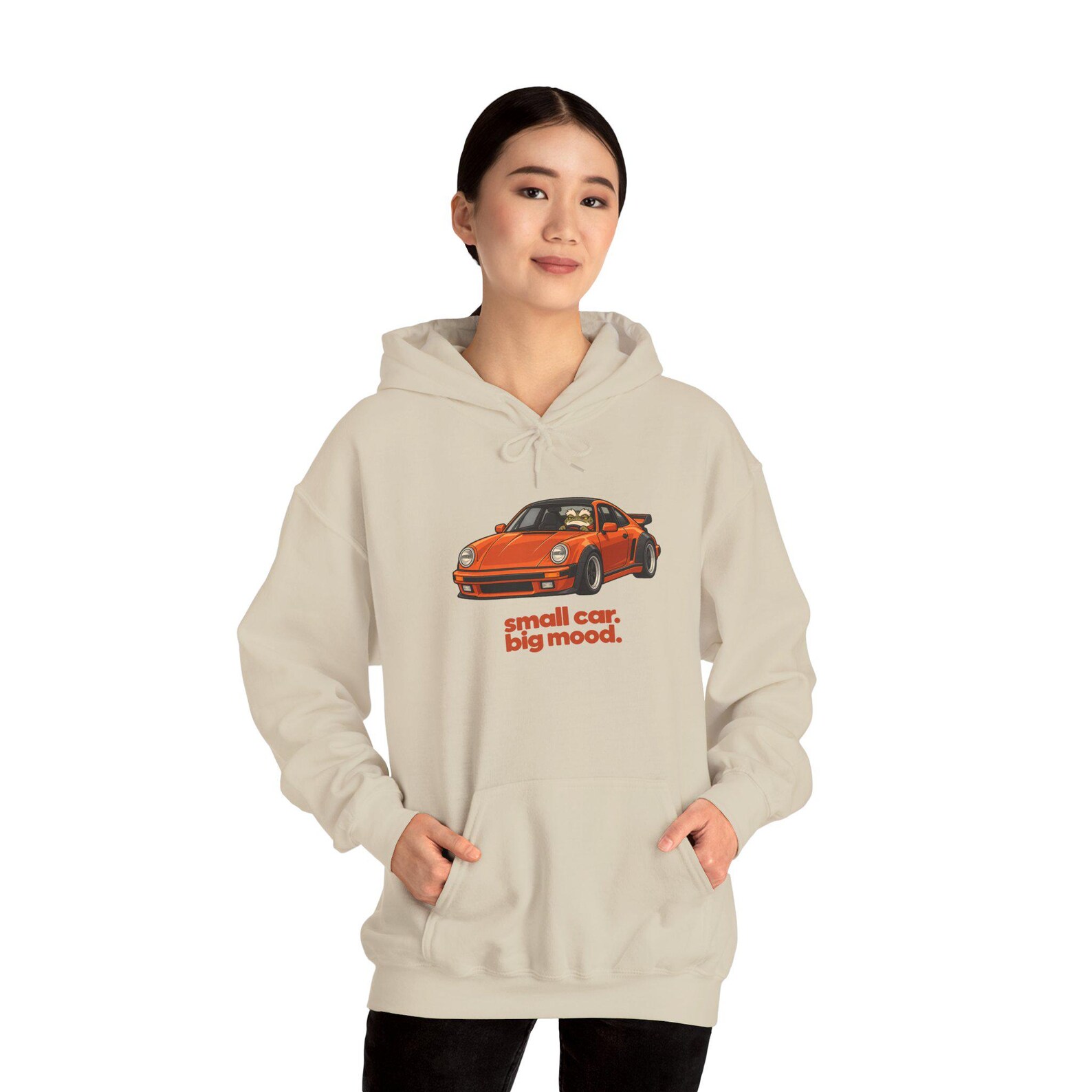Model wearing a sand BRUMTOAD graphic hoodie with an orange car and the words Small car. Big mood.